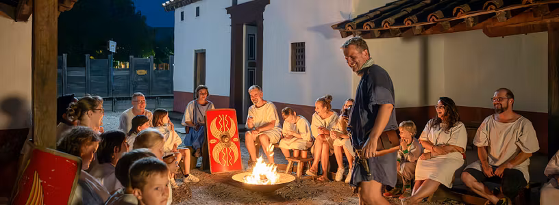 Römisch gekleidete Männer und Frauen nachts an einem Lagerfeuer in historischer Kulisse