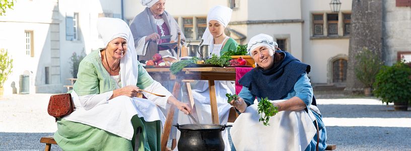Eine Gruppe historisch gekleideter Frauen kochen im Hof von Schloss Lenzburg.