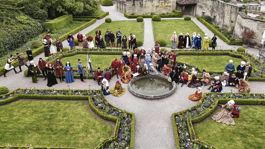 Eine grosse Gruppe Menschen, die mittelalterlich gekleidet sind, stehen imn einem grossen Garten. Luftaufnahme mit Drohne. Gruppenbild