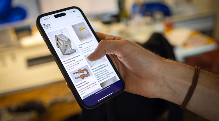 Grosses Handy in der Hand eines Benutzers, auf dem Bildschirm ist die "Sammlung online" von Museum Aargau dargestellt.