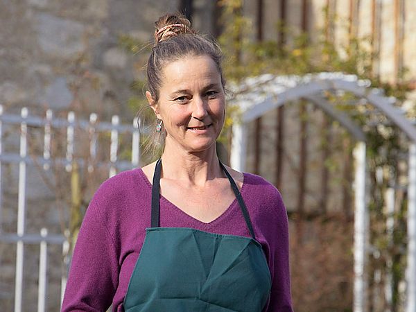 Eine Frau mit Gärtnerkleidung steht in einem Garten.