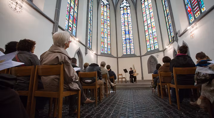Blick in den Chor der Klosterkirche Königsfelden mit ihren Glasfenstern. Vorne auf der Bühne spielt eine Musikerin, der Chor ist gefüllt mit Zuhörerinnen und Zuhörern.