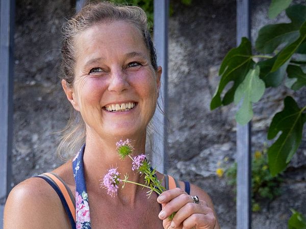 Porträt von Gärtnerin Tanya van der Laan. Sie befindet sich im Garten von Schloss Wildegg und hält gepflückte Blumen in der Hand. Im Hintergrund befindet sich eine Mauer mit einem Gitter.