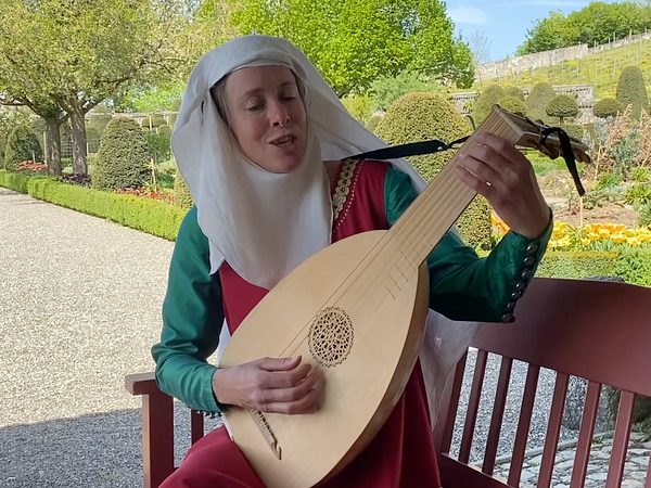 Eine mittelalterlich gekleidete Person spielt eine Laute im Garten von Schloss Wildegg.