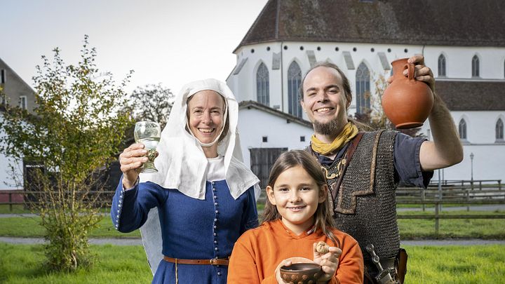Eine mittelalterlich gekleidete Frau, ein römischer Legionär sowie ein modern gekleidetes Mädchen. Sie blicken alle freudig in die Kamera.