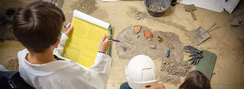 Kinder als Forscherinnen und Forscher verkleidet begutachten die Ausstellung und lösen Rätsel (Aufnahme von Oben)