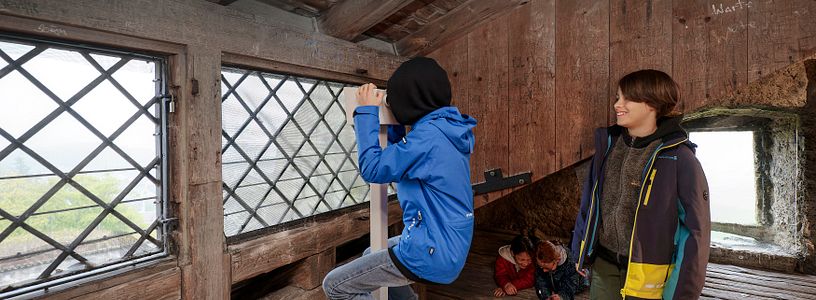 Zwei Schüler unter dem Dach von Schloss Habsburg; ein Bub blickt durch ein Fernrohr ins Weite.