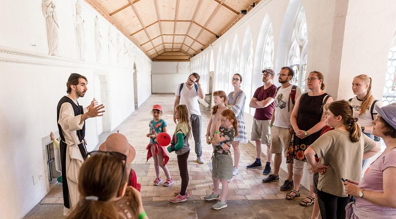 Ein als Mönch gekleideter Museumsvermittler steht mit Besucherinnen und Besuchern im Kreuzgang des Klosters Wettingen