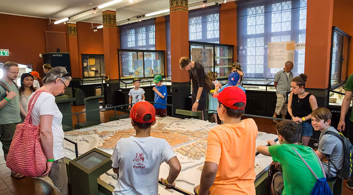 Besucherinnen und Besucher, mit dabei auch Kinder mit roten Käppis, betrachten auf einer Führung im Vindonissa Museum ein grosses Modell des ehemaligen Legionslagers. 